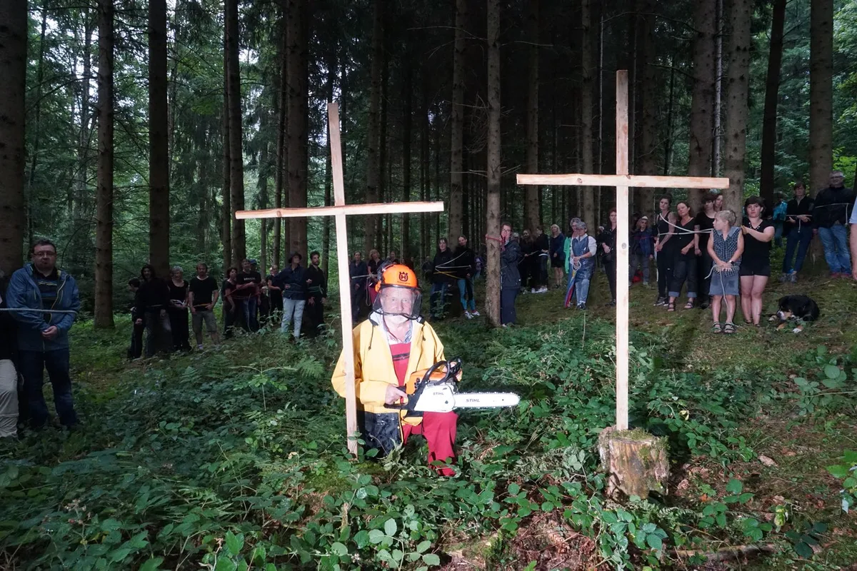 Protestierende Menschen mit Motorsäge und symbolischen Grabkreuzen im Wald.